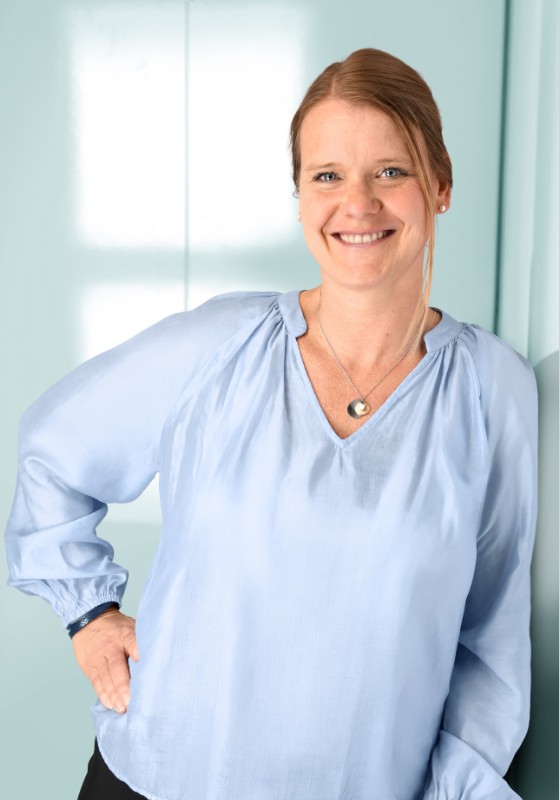Portrait eines netten Mannes im mittleren Alter mit kurzen braunen Haaren und Anzug, der vor hellblauem Hintergrund lächelt